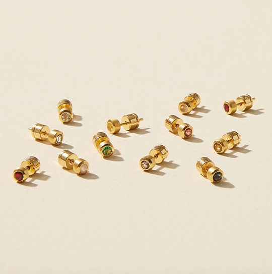 Assortment of Dean Davidson Gold earring studs with gemstones on a beige background